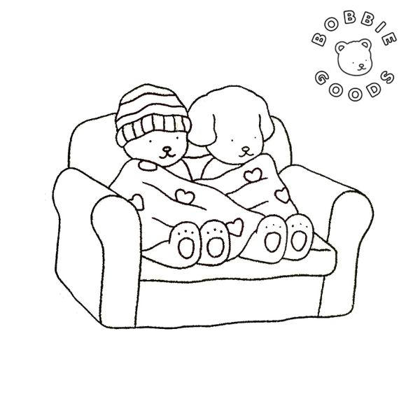 Desenho da Bobbie Goods com um ursinho de gorro e um cachorro no sofá, cobertos por um cobertor de corações, ideal para colorir e celebrar a amizade.